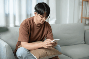 A man sitting on a sofa using his smartphone, depicting the common mobile-first behavior of customers searching for "restaurants near me" or browsing food delivery apps.