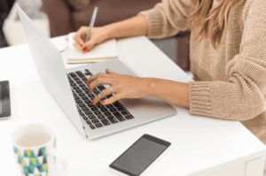 A restaurant owner or marketer typing on a laptop and taking notes on a white desk, representing the process of managing local SEO and digital marketing for a Singapore restaurant.