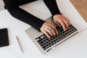 Overhead view of a business owner typing on a laptop with a smartphone nearby, representing the process of contacting Google Support or updating business details.