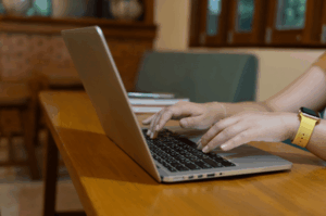 A close-up of a person's hands with a yellow smartwatch typing on a laptop keyboard. This represents the active process of contacting Google support or updating business information to fix visibility issues.