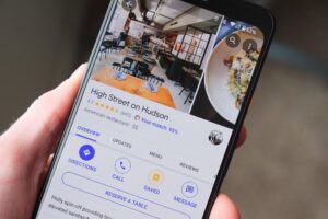 A hand holds a smartphone displaying a Google Maps profile for a restaurant called High Street on Hudson.