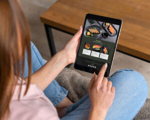 A woman focused on a tablet screen showing a sushi restaurant website, highlighting her interest in browsing food options and discovering dining experiences online.