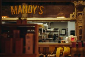 The storefront window displays the name "MANDY'S" in bold, yellow letters above a busy service counter filled with order receipts.