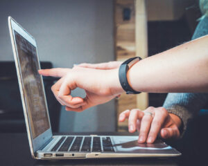 Two people pointing at a laptop screen together, discussing or reviewing information on the display.