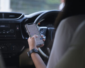 A woman driving a car while glancing at Google Maps on her phone, using the navigation app to follow directions during her journey.