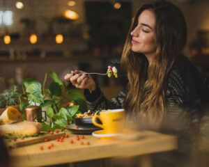 A woman enjoying her meal at a restaurant, seated at a neatly set table with soft lighting and a calm, pleasant ambience.