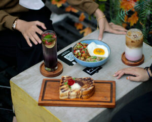 Two women sitting at a café table, smiling and talking while enjoying their meals, with plates of food and drinks in front of them, conveying a friendly and casual dining experience.