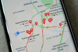A smartphone displays a Google Maps view of the Bayan Lepas area in Penang, Malaysia, with several restaurant markers and the Snake Temple highlighted.