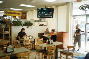 The image depicts the interior of a casual diner or "Giant Burger" restaurant, where a few patrons are seated at small tables with condiments and napkins.
