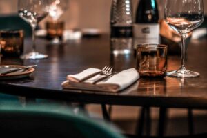 An elegant dinner table is set with wine glasses, amber-colored tumblers, and folded napkins. Warm, low lighting creates a sophisticated and intimate atmosphere in the dining room.