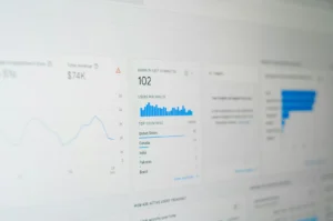 A digital analytics dashboard displays data with graphs and charts. Key elements include 102 users per minute, revenue of $74K, and top countries like the U.S. and Canada.
