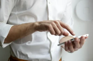A person in a white shirt uses a smartphone, focusing intently as fingers tap the screen. The setting is bright, conveying a modern, professional tone.