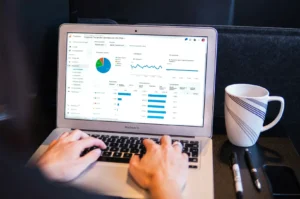 A person types on a laptop displaying analytics graphs. A coffee cup and pens are nearby. The setting is relaxed yet focused, suggesting productivity.