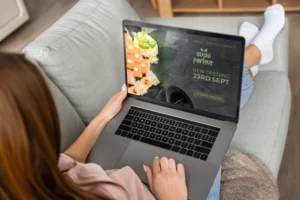 A woman rests on a sofa while holding a laptop in her lap. Her screen displays a promotional website for a restaurant called "Sushi Parlour.”