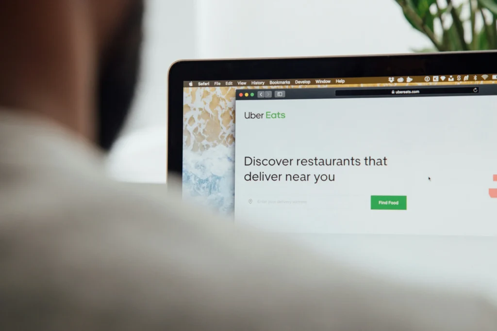 A person looks at a laptop screen displaying the Uber Eats website homepage. The screen shows the logo alongside the heading "Discover restaurants that deliver near you.”
