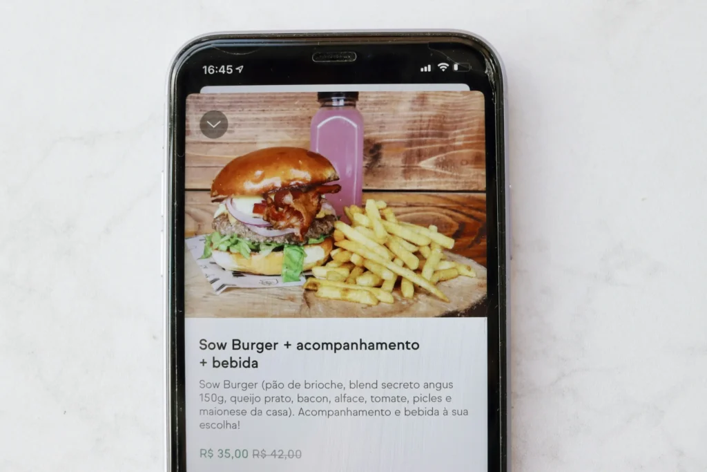 A smartphone screen displays a food delivery app listing for a meal combo. The top photo shows a beef burger topped with bacon and lettuce next to French fries and a bottle of purple drink.